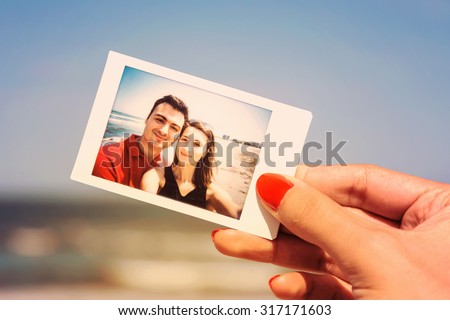 Retro Photo Of Girl Hand Holding Instant Photo Of Happy Couple On Beach