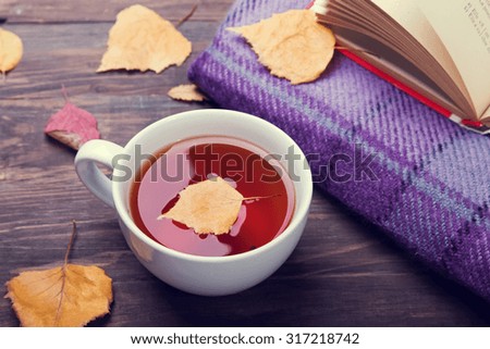 Cup of tea, autumn leaves and blanket on the wooden table. Toned photo.