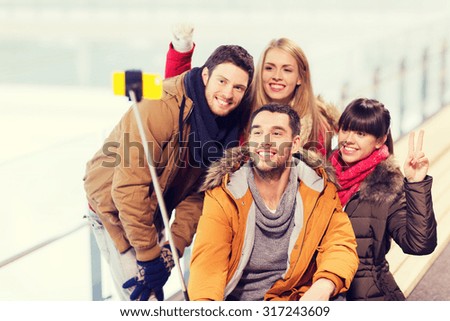 people, friendship, technology and leisure concept - happy friends taking picture with smartphone selfie stick on skating rink