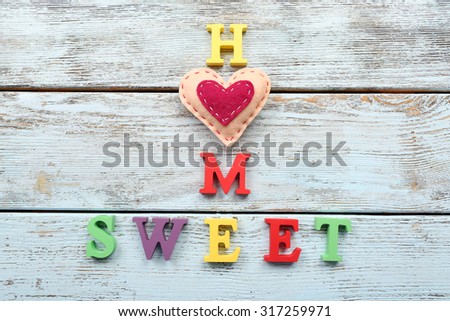 Decorative letters forming words SWEET HOME with heart on wooden background