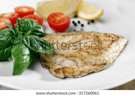 Dish of fish fillet with basil and lemon on plate close up