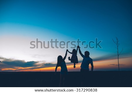 Happy family together, parents with their little child at sunset. Father raising baby up in the air. Royalty-Free Stock Photo #317290838