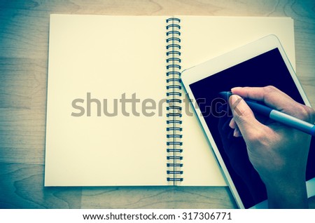 Hand writing by pen mouse on Tablet with open leather book over wooden background