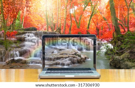 Conceptual image of a computer laptop on Beautiful waterfall with soft focus and rainbow in the forest