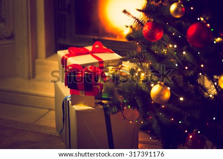 Toned photo of decorated Christmas tree and gift boxes against burning fireplace