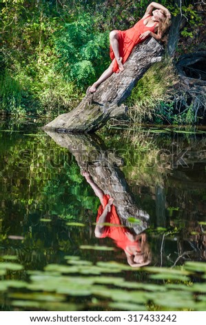 girl in a red dress lying on an old tree trunk.