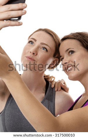 Two fitness women take a selfe picture on a mobile phone at the gym 