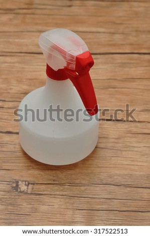 A white spray bottle with a red trigger isolated against a wooden background