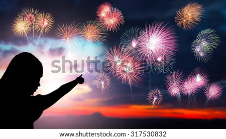 The silhouette of a young girl watching a fireworks display during sunset. Beautiful firework display for celebration. Sunset background. Sunset with firework background. Hand pointed fireworks.