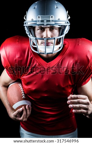 Portrait of confident American football player running while holding ball against black background