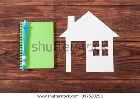 White paper house figure with notebook on wooden background.