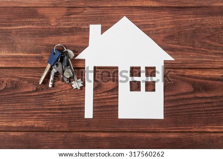 White paper house figure with silver keys on wooden background.