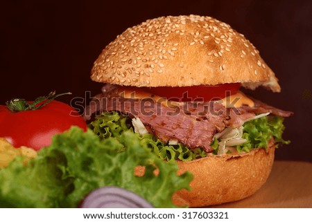 One big tasty appetizing fresh burger of green lettuce red tomato cheese bacon slice meat cutlet violet oinion and white bread bun with sesame seeds on black background closeup, horizontal picture