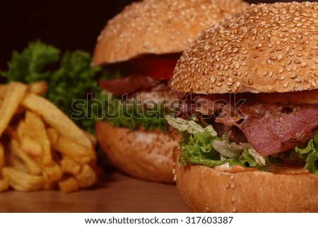 Few big tasty appetizing fresh burgers of green lettuce red tomato cheese bacon slice meat cutlet violet oinion white bread bun with sesame seeds and chips on wooden table closeup, horizontal picture