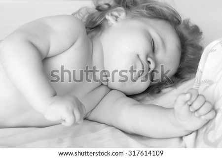 Closeup view of one sweet small sleeping boy child with blonde curly hair round cheeks and tiny fingers lying with closed eyes in bed black and white, horizontal picture