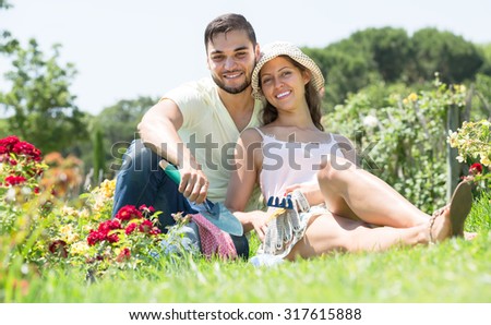 Portrait of young happy couple resting after work in flower garden
