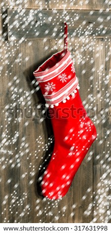 Christmas stocking. Red sock with snowflakes for Santa gifts hanging over rustic wooden background and falling snow effect