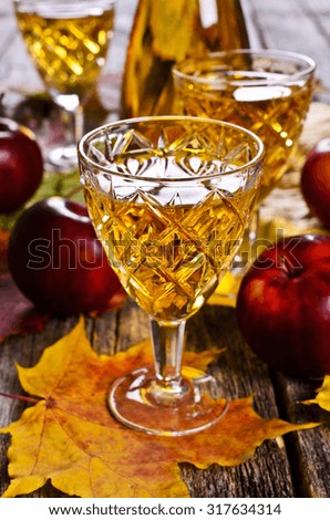 Apple drink in a transparent glass on a wooden surface on a background of red apples and maple leaves