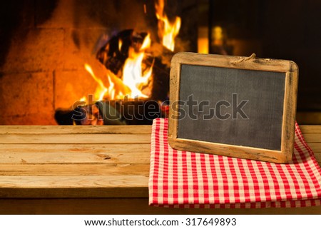 Chalkboard on wooden table over fireplace background. Winter and Christmas holiday concept