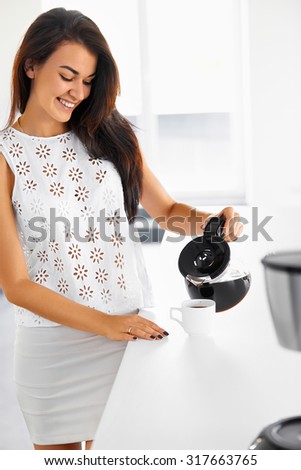 A picture of a young happy woman pouring coffee to a white mug in the kitchen