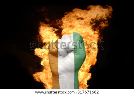 fist with the national flag of cote divoire near the fire on a black background