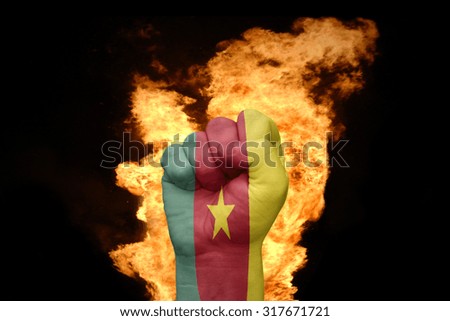 fist with the national flag of cameroon near the fire on a black background