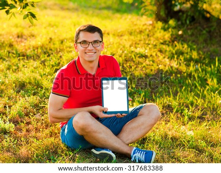 Young man using tablet computer on autumn  park. Man holding and shows touch screen tablet pc with blank screen