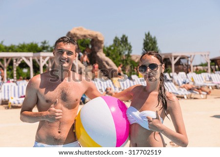 Portrait of Happy Young Couple Posing on Beach with Striped Beach Ball Giving Thumbs Up Sign to Camera on Sunny Summer Day While on Vacation
