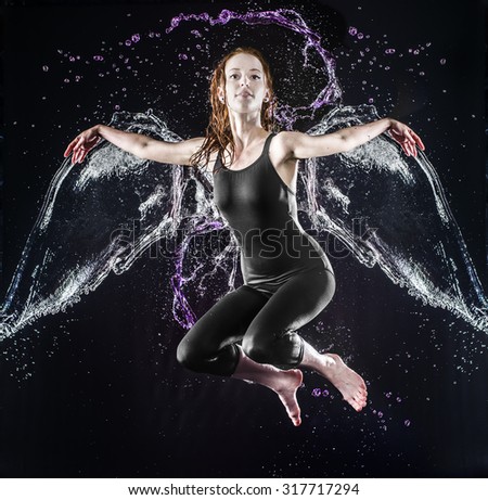 Young Woman with Water Wings Floating in the Air with Splashes and Looking at the Camera Against Black Background.