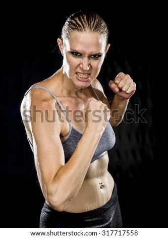 Close up Athletic Woman in Combat Pose Looking Aggressive at the Camera Against Black Background.