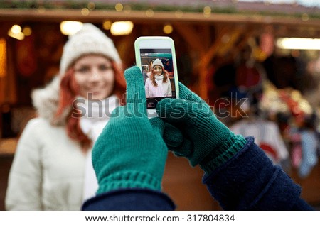 holidays, winter, christmas, technology and people concept - happy couple of tourists in warm clothes taking picture with smartphone in old town