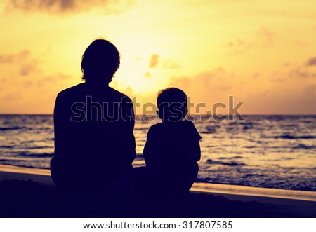 silhouette of father and little son looking at sunset on beach