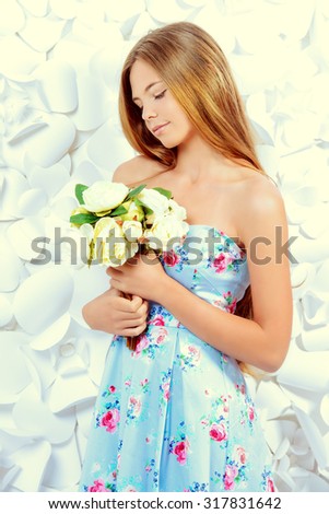 Romantic smiling girl posing in summer dress by a background of white paper flowers. Beauty, fashion.