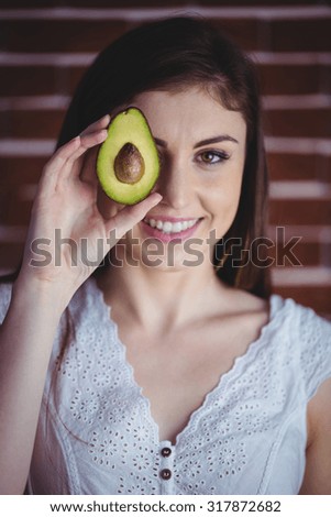 Woman showing fresh avocado on red brick background