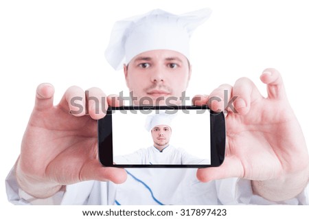 Chef or cook taking selfie with back phone camera showing his face on the screen or display