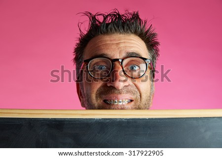 Nerd man crazy behind a blackboard and braces smile funny gesture in pink background