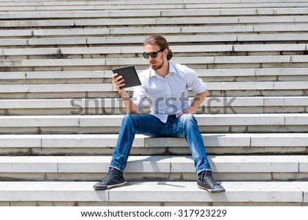 Young man sitting on stairs looking at digital tablet