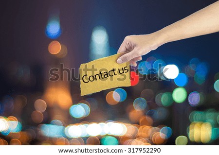 Hand holding a Contact us sign made on sugar paper with city light bokeh as background