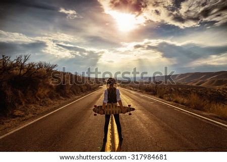 young woman resting with longboard on a hill overlooking the city below in the valley during sunrise or sunset with a toned vintage retro instagram filter