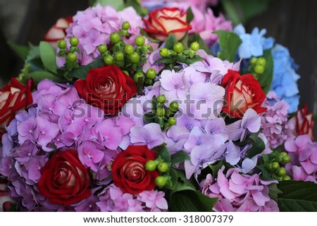 Closeup of beautiful fresh colorful summer bunch of cut flowers with red roses voilet and blue hydrangea and green buds, horizontal picture