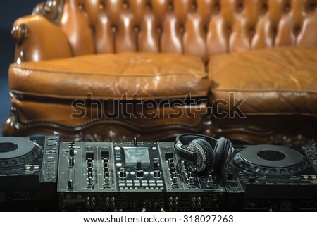 Front view of dj musical mixer professional black console with many buttons and knobs and glamour headphones with pastes in night club or studio on brown leather sofa background, horizontal picture