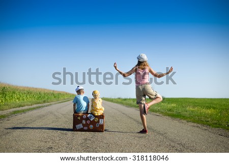 Picture of young woman meditating and two children sitting on old suitcase on country road. Backview of family traveling and waiting on blue sky sunny outdoors background.