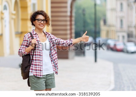 Think positively. Pleasant blissful young girl holding her bag and thumbing up while feeling elated