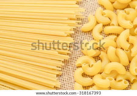 Raw Spaghetti and elbow macaroni. Italian Pasta raw food collection on sack background.