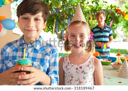 Close up portrait of happy children together, celebrating a colorful birthday party in home garden, home outdoors. Proud boy holding birthday cupcake with candle. Kids fun active lifestyle, exterior.