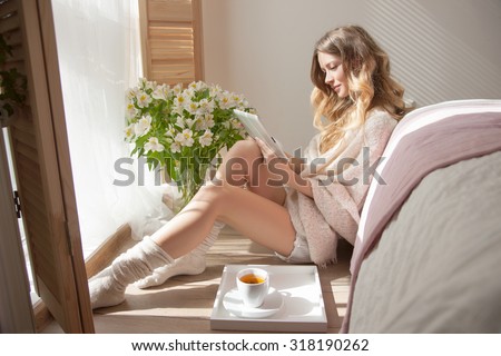 Flowers in Women's Bedroom, Fragrance evokes a Woman. Sun is shining into the Bedroom, girl is reading on the background of flowers. Cozy image, attractive Model in the Morning, Relaxing day         
