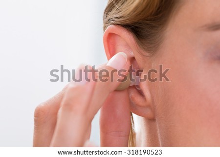 Close-up Of Female Hands Putting Hearing Aid In Ear
