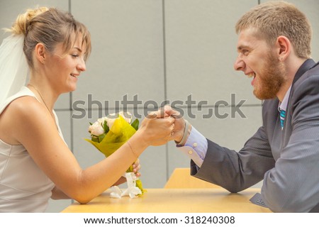 Bride and groom sitting at a table in the cafe and fight. Armwrestling