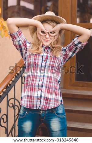 Girl wearing cowboy hat making glasses by hands in countryside