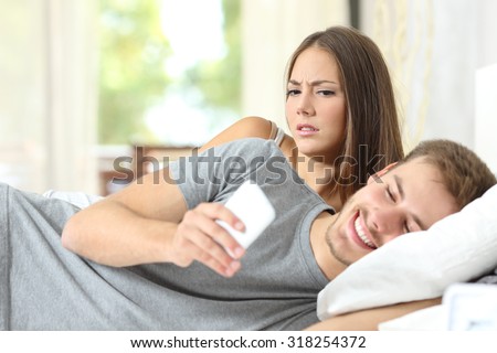 Jealous woman spying her husband mobile phone while he is reading a message Royalty-Free Stock Photo #318254372